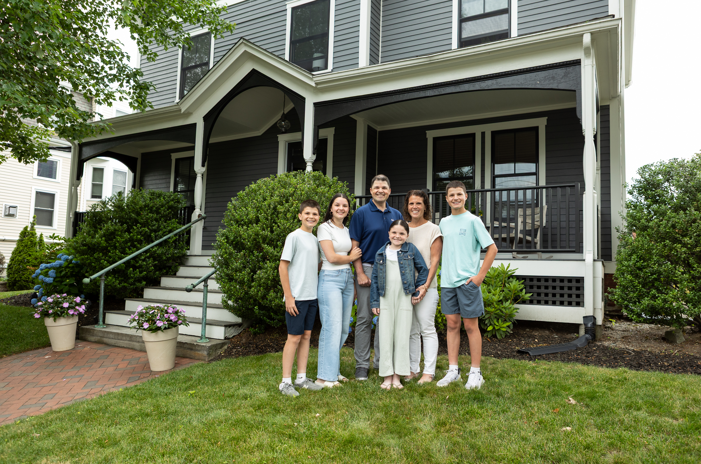 Family of six standing in the front yard of a colonial home.