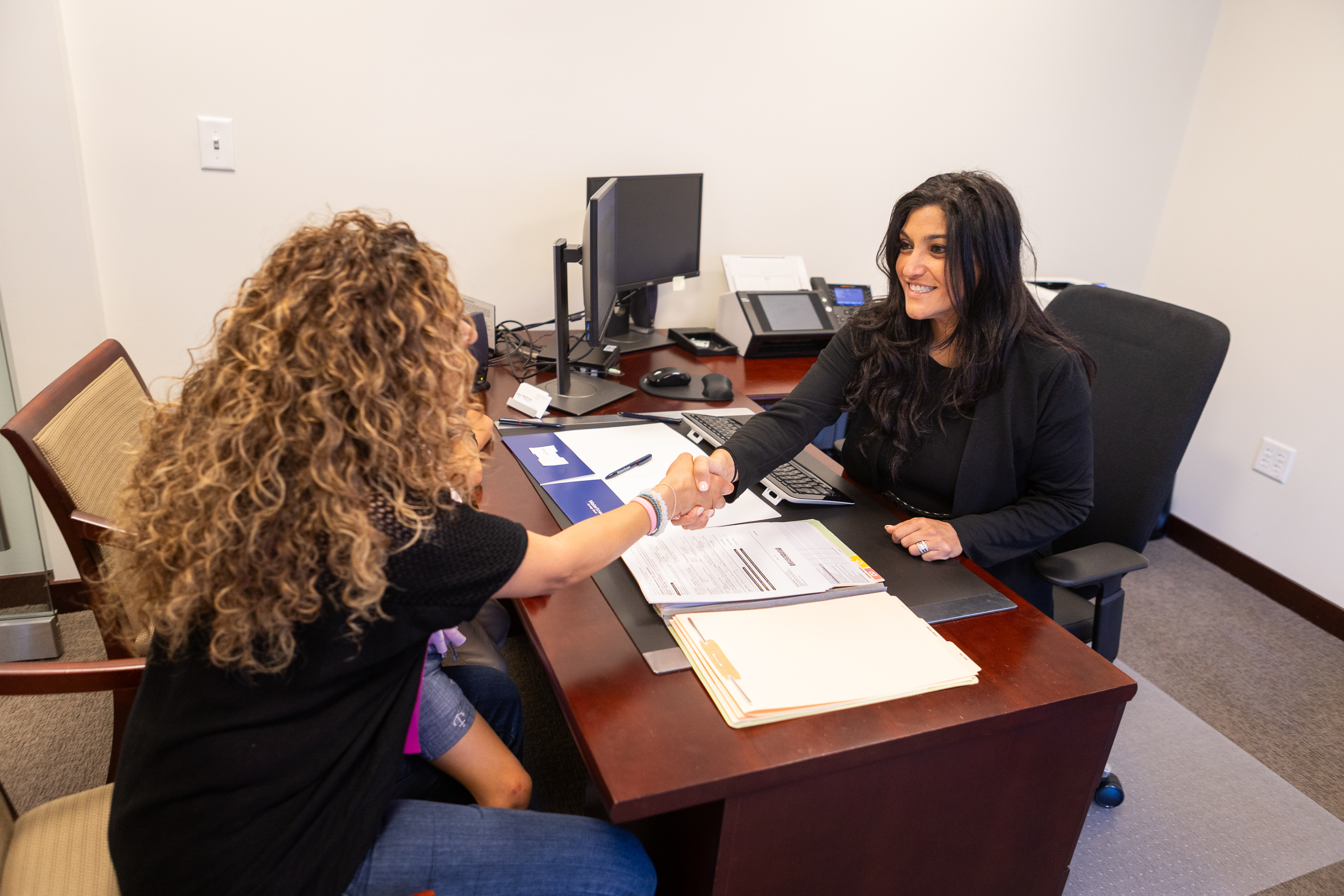 A Loan Officer meeting with a customer and shaking hands over a set of documents on the desk.