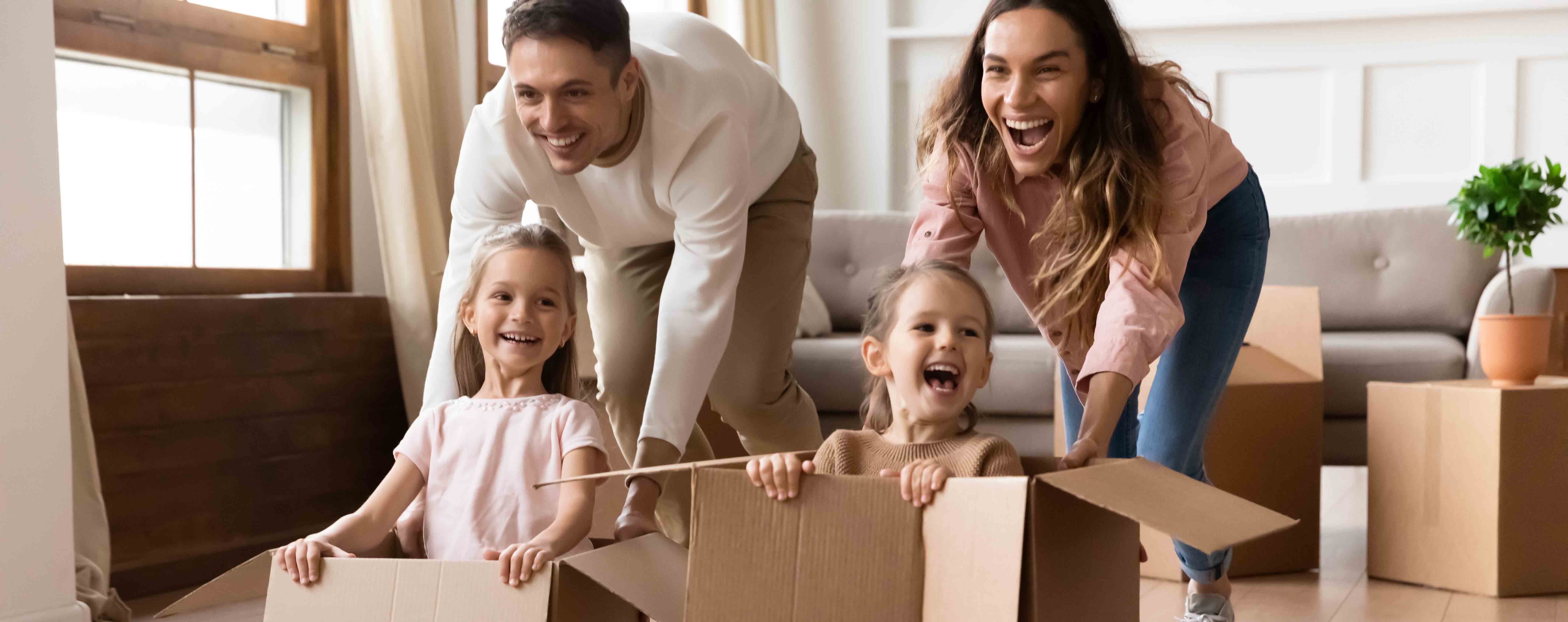 Young parents pushing their daughters in cardboard boxes
