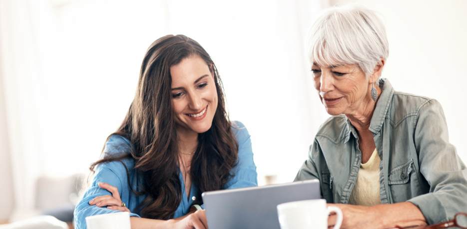 Young woman helping an older woman on the laptop.