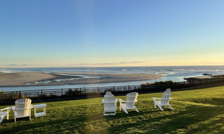 Adirondack chairs on a green lawn overlooking water.