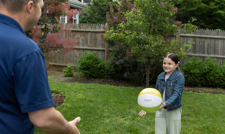 A father and daughter playing with a beach ball in their backyard.