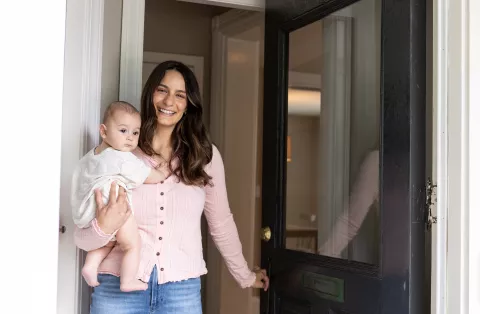Mom holding a newborn while opening the door to her new home.