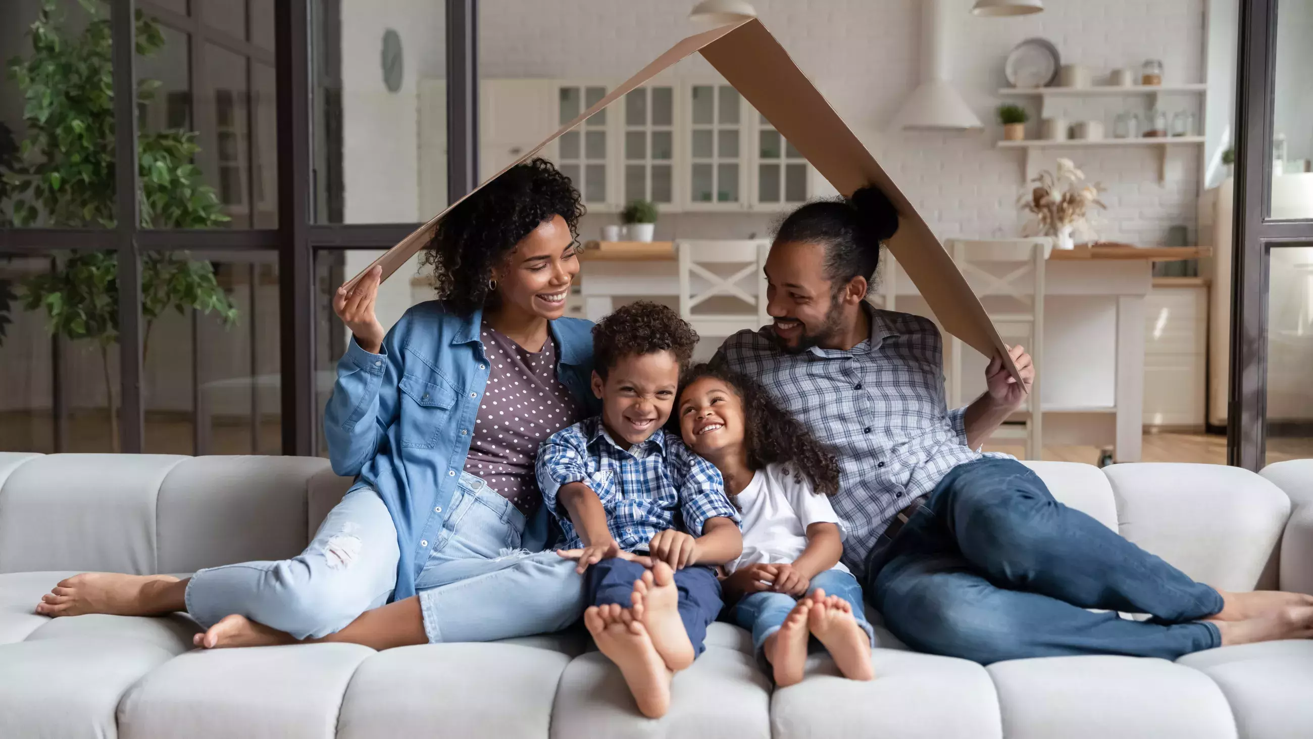 Young family sitting on a couch with cardboard over their heads like a home