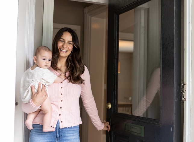 Mom holding a newborn while opening the door to her new home.