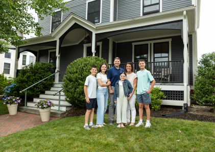 Family of six standing in the front yard of a colonial home.