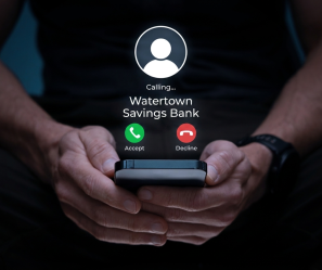A person holding a phone with an incoming call from Watertown Savings Bank and two buttons 'accept' or 'decline'