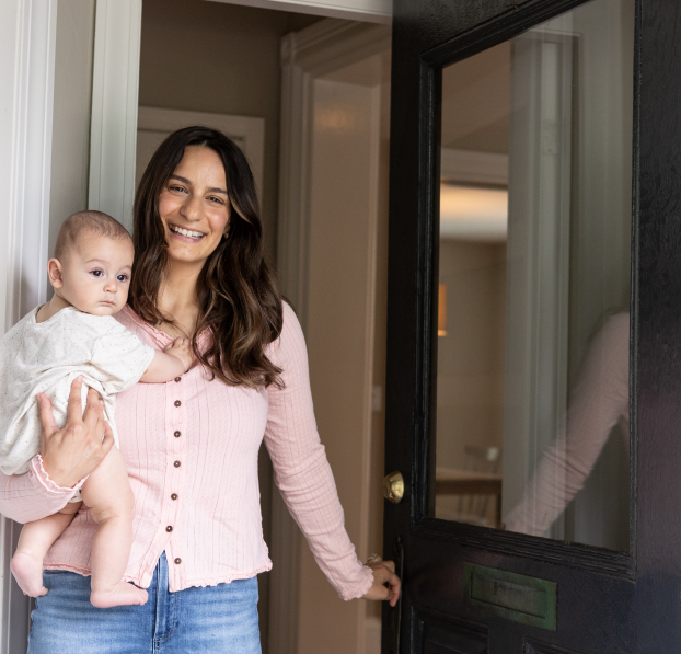 Mom holding a newborn while opening the door to her new home.