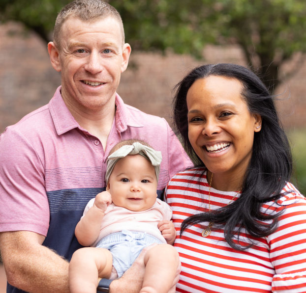 Young family holding their baby and posing to the camera in front of Watertown Savings Bank.