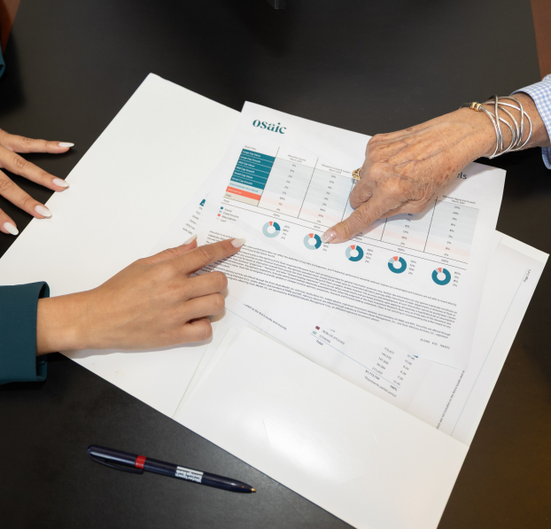 Two persons' hands pointing to information on documents with charts and graphs.